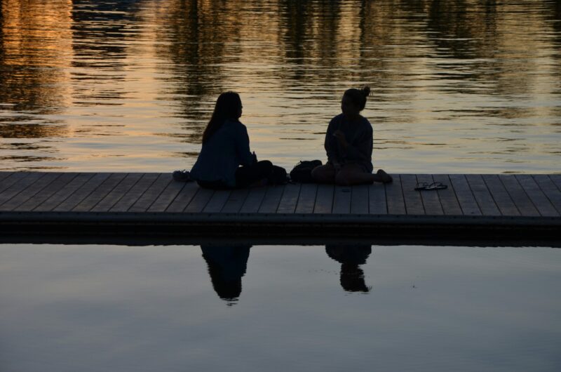 Two people sitting together on a dock at sunset